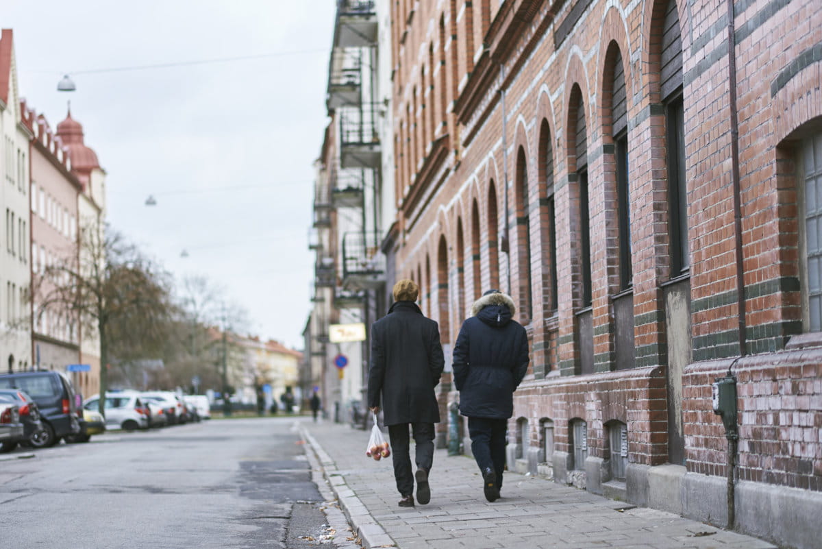 Dwie osoby idą chodnikiem przy kamienicy
